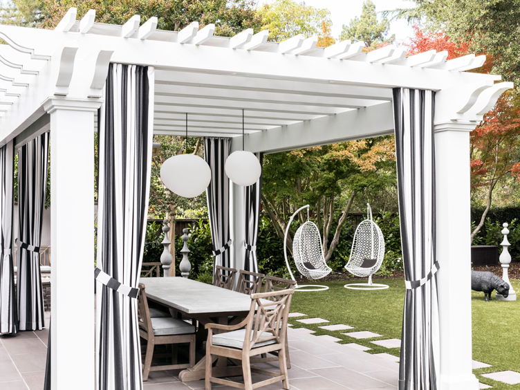 farmhouse table and chairs under outdoor structure with white hanging birdcage chairs.