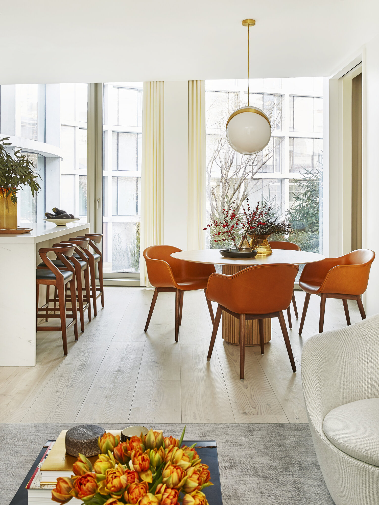 Bright dining room with wood pedestal table with orange leather dining chairs and globe ceiling light