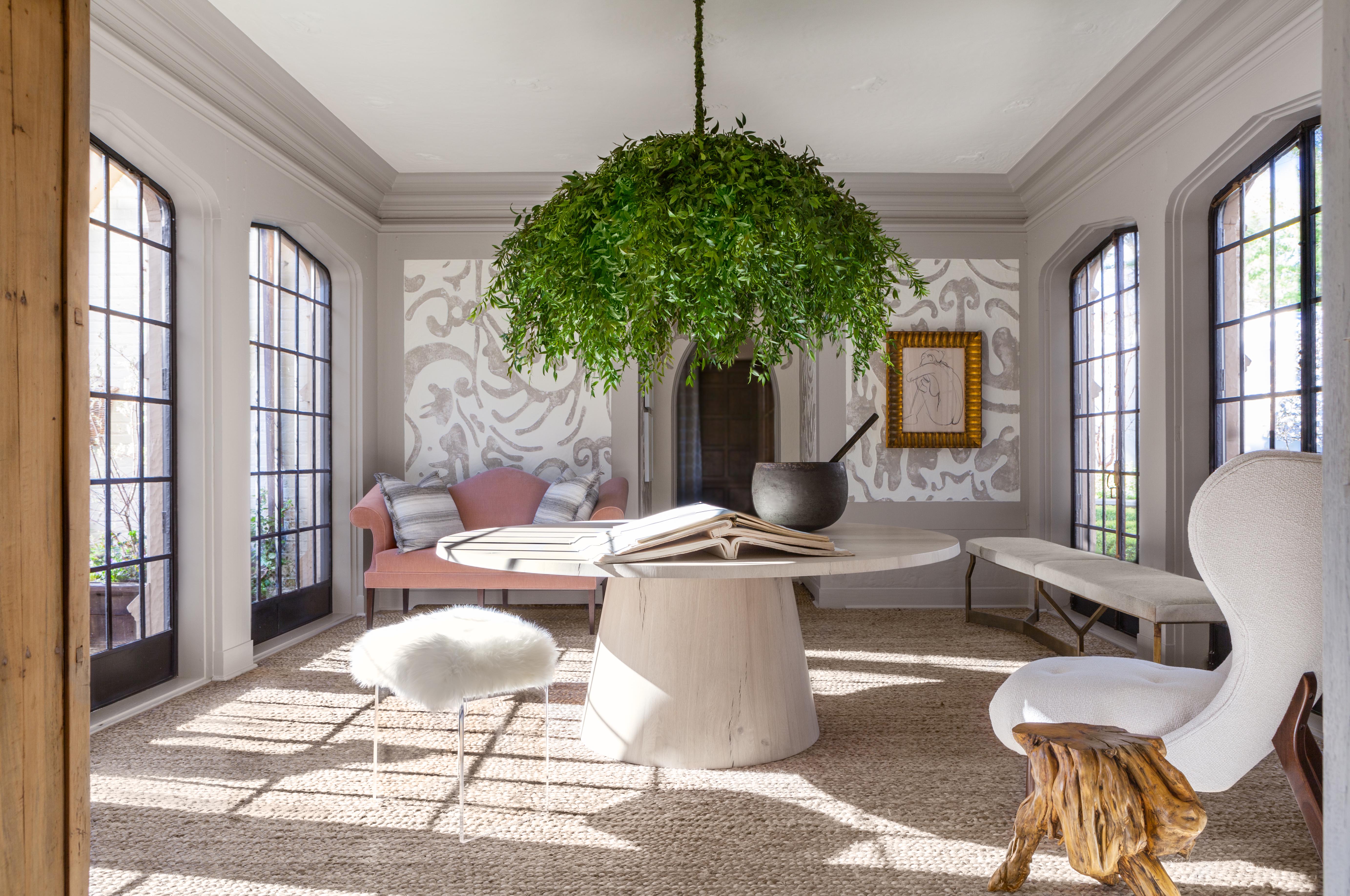 Sitting room with large pedestal table, minimalist furniture, and a large chandelier-like hanging plant.