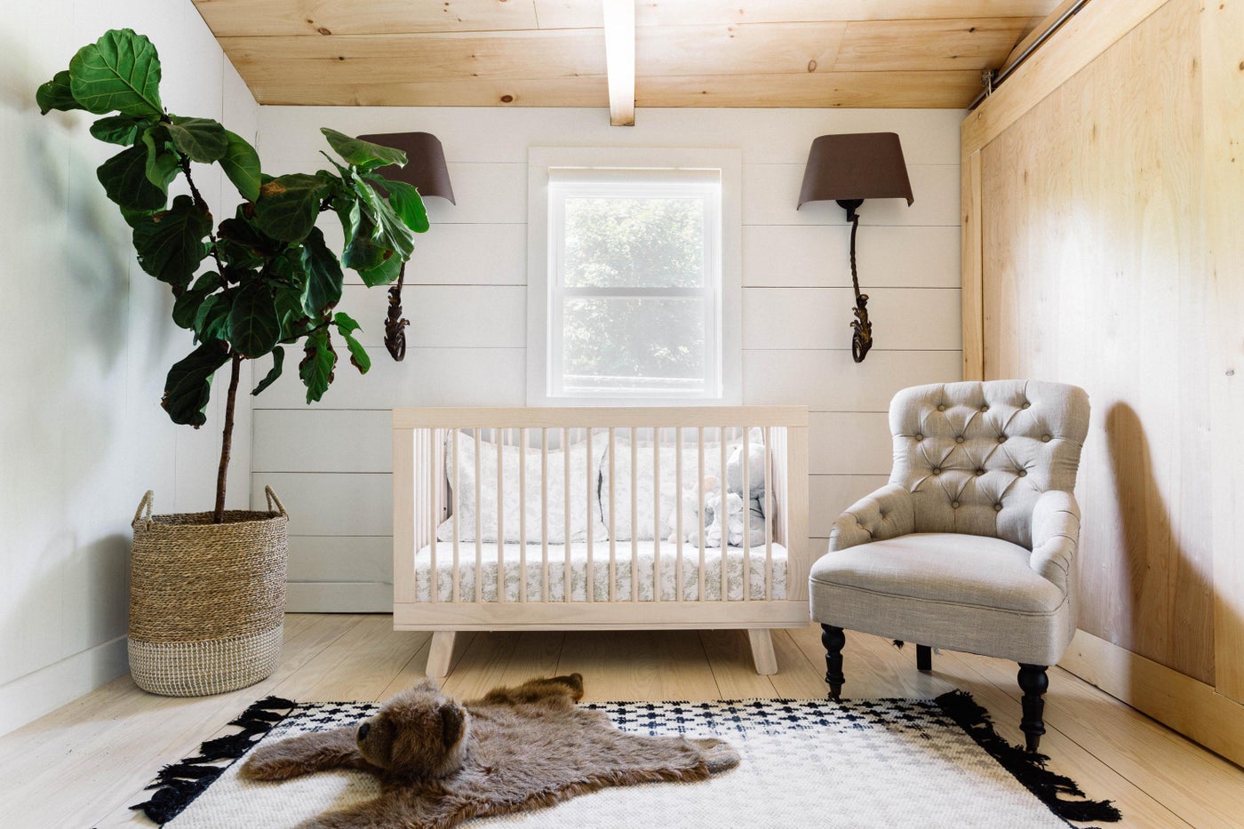 Nursery with raw wood crib, faux bear skin rug, and fiddle leaf fig in woven basket.