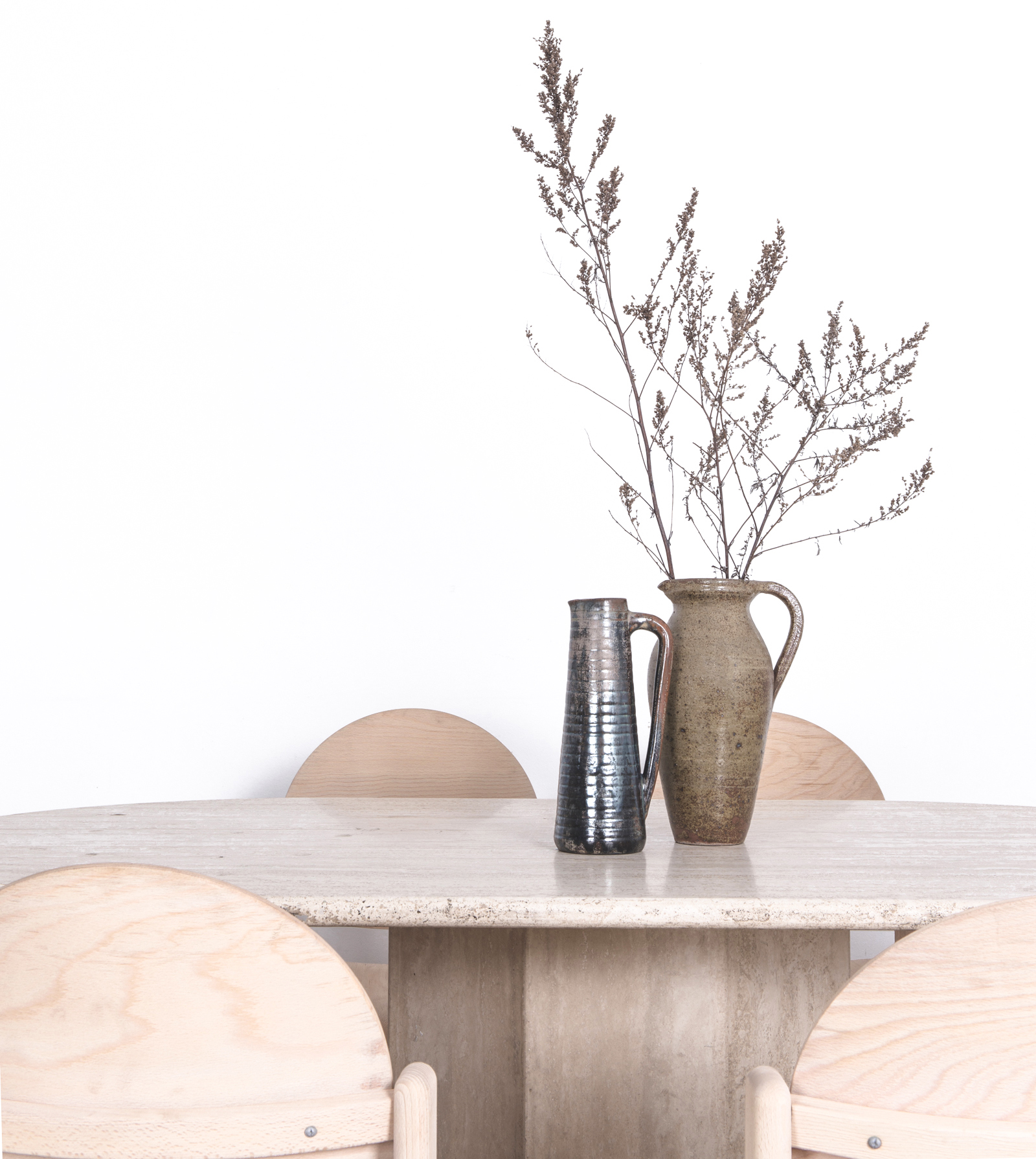 Two ceramic vases on a stone pedestal dining table with raw wood dining chairs