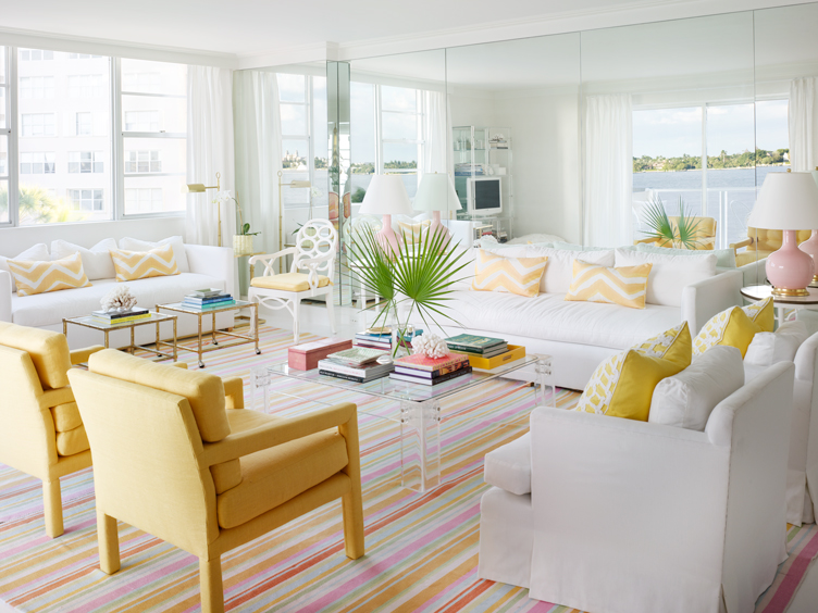 Bright, beachy living room with colorful striped rug, lucite coffee table, and yellow armchairs.