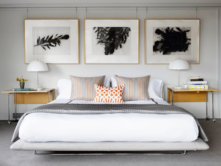 Modern bedroom with wood side tables, 60's table lamps, and three hanging photographs.