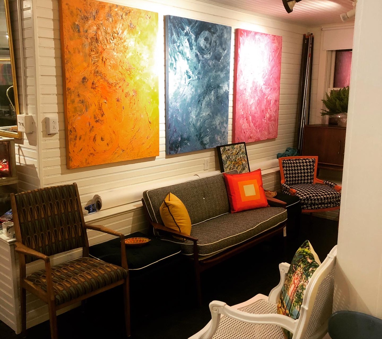 Mid-century style armchair and sofa under colorful, textured paintings