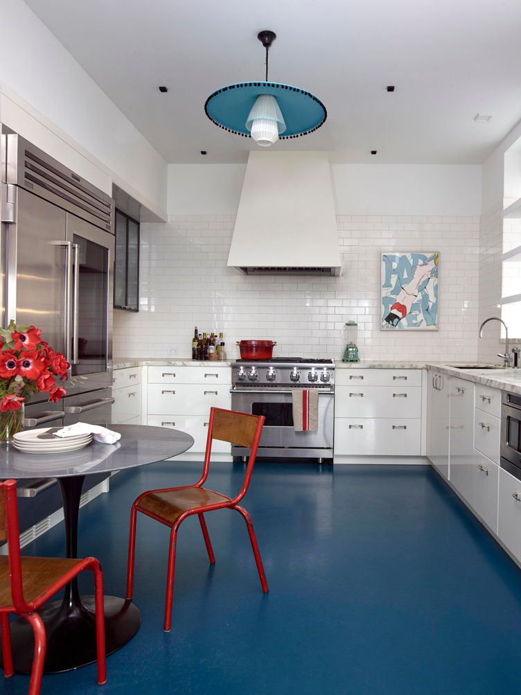 Kitchen with subway tiles, blue floors, a tulip table, and red industrial-style chairs.