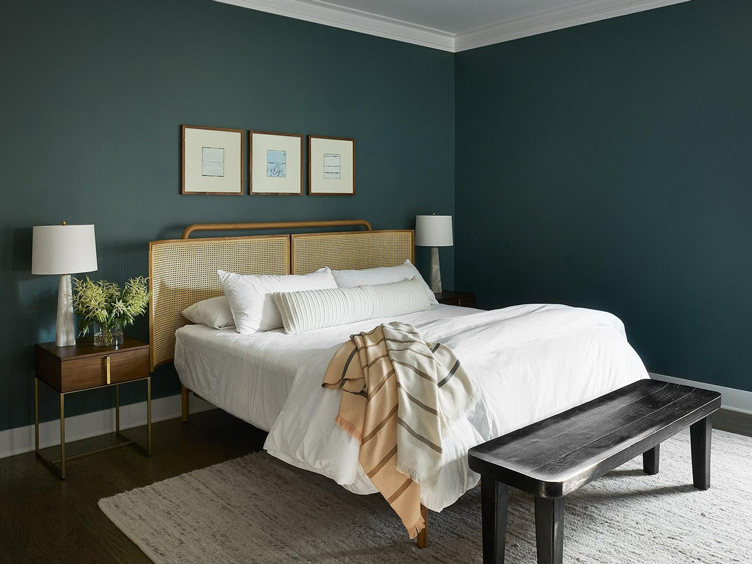 The dark teal walls in this bedroom compliment the black wood bench and light rattan headboard.