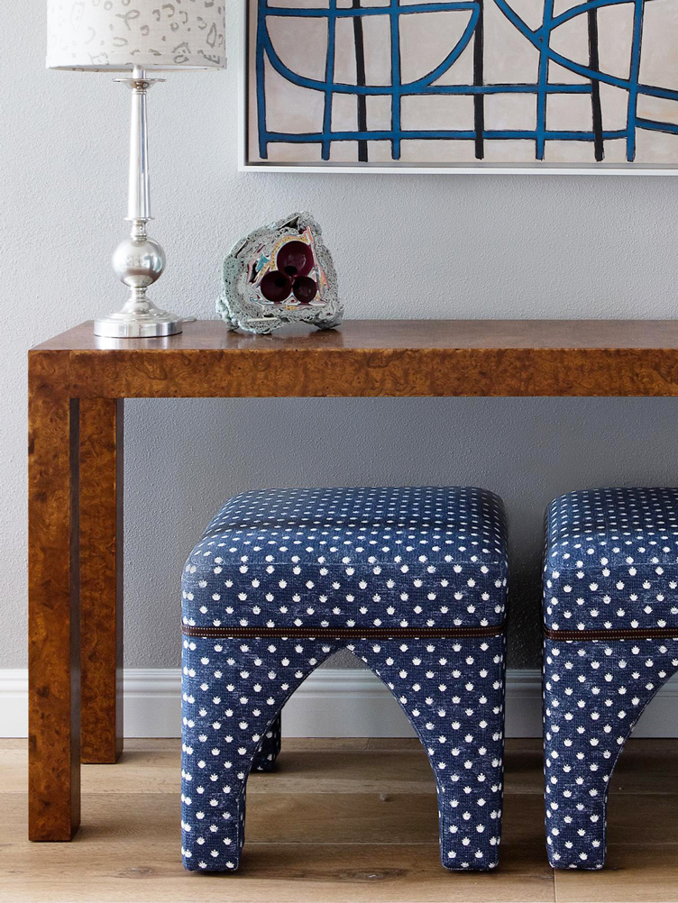 Burl wood side table with silver lamp, blue, polka-dot stools, and blue painting 