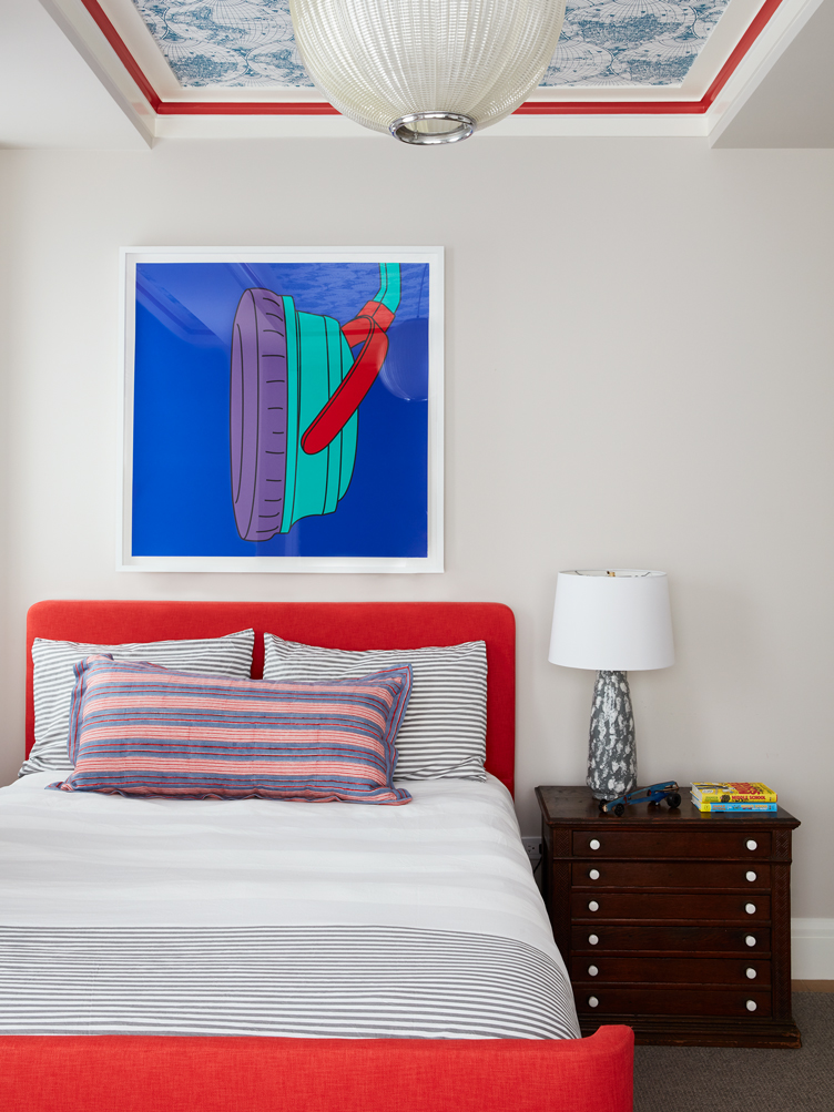 Kids room with classic wood side table, bright red headboard and colorful pop-art style painting.