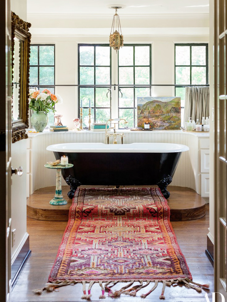 Red textile rug leads up to wooden platform with black clawfoot tub 