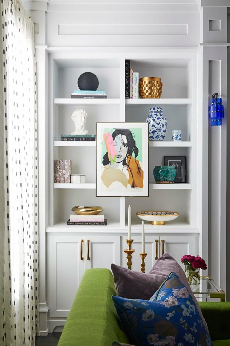 White built-in bookshelves with ceramics and framed picture next to a green sofa