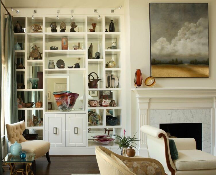 White bookshelves with mirrored backs and traditional white marble fireplace with large painting