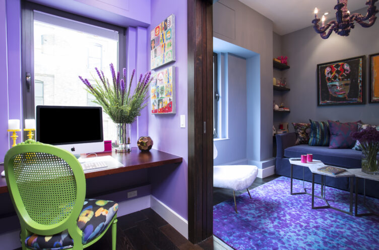 Eclectic office and seating area with purple walls, lime green rattan desk chair, and purple rug.