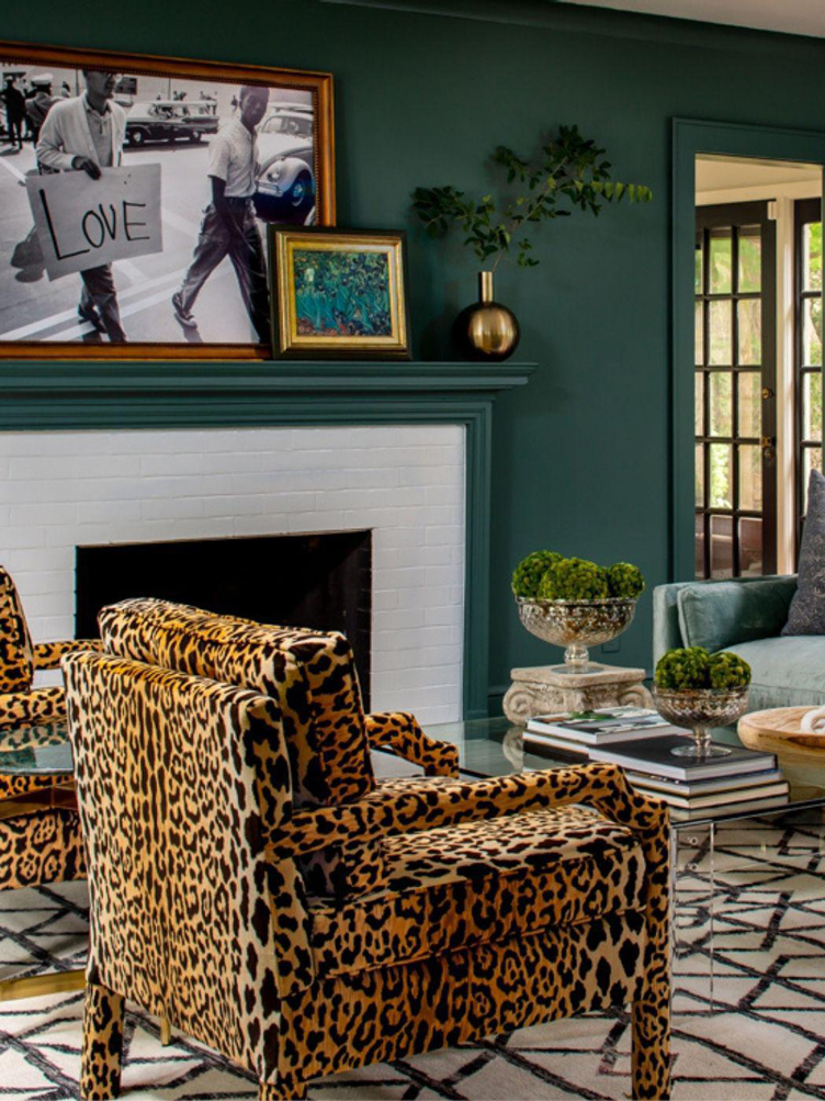 Green living room with cheetah armchairs and layered framed pictures over the brick fireplace