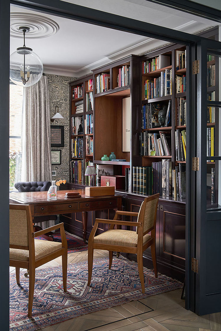 This office with graphic wallpaper and built-in shelves features a classic wood desk