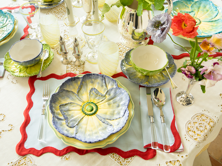 Maximalist dining set with ceramic flower plates and bowls and red-trim tablecloth 