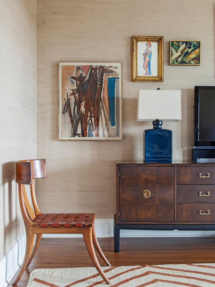 Leather woven chair in room with textured wallpaper and framed paintings