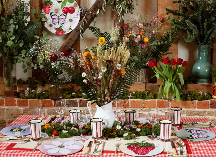 Bell Hutley tables cape with mismatched bug and fruit plates, enamel cups, and floral centerpiece.