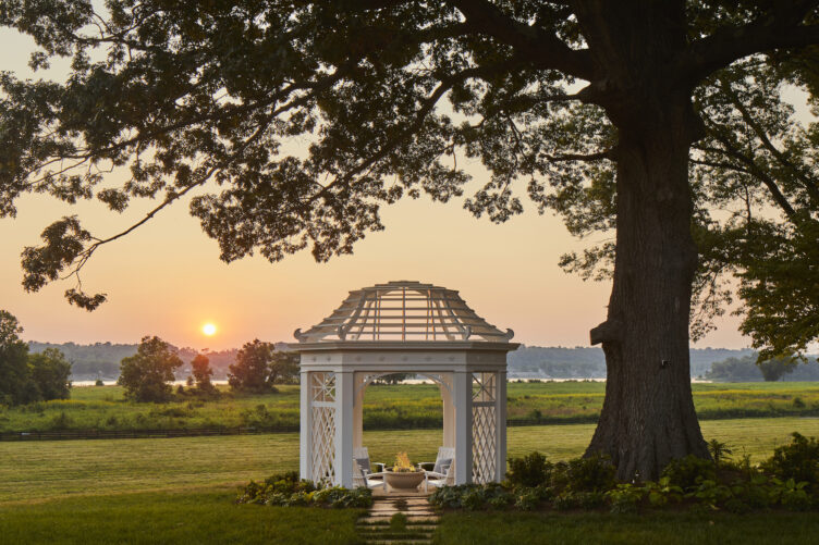 The fire pit, surrounded by white Adirondack-style chairs, sits under a gazebo-like structure.