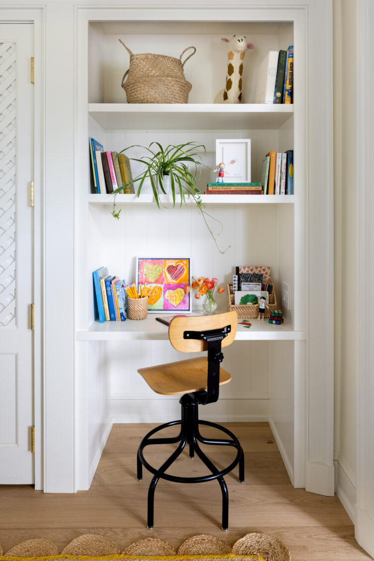 Kid's desk nook with white built-in shelves and wooden and metal swivel chair.