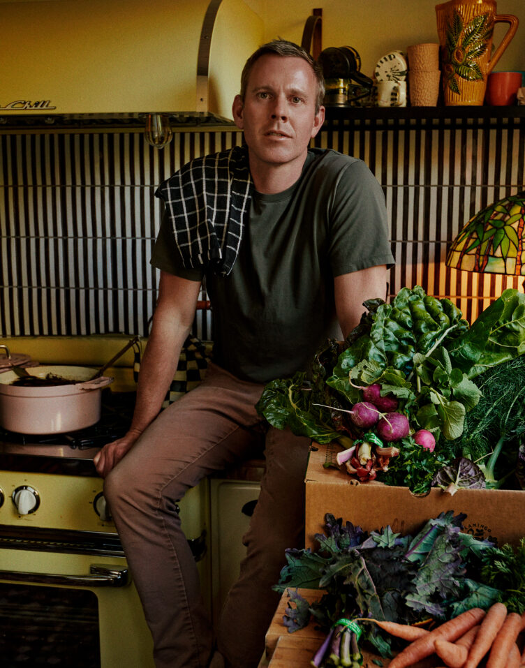 Richard Christiansen sits in kitchen with vintage chartreuse stove and black and white backsplash 