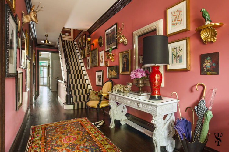 Pink hallway with white ornate side table, patterned rug, black and white table runner, and framed paintings.