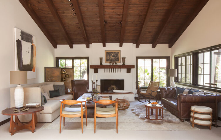 Living room with dark wood ceiling and accents, brown tufted leather couch, and mid-century wood accent chairs.