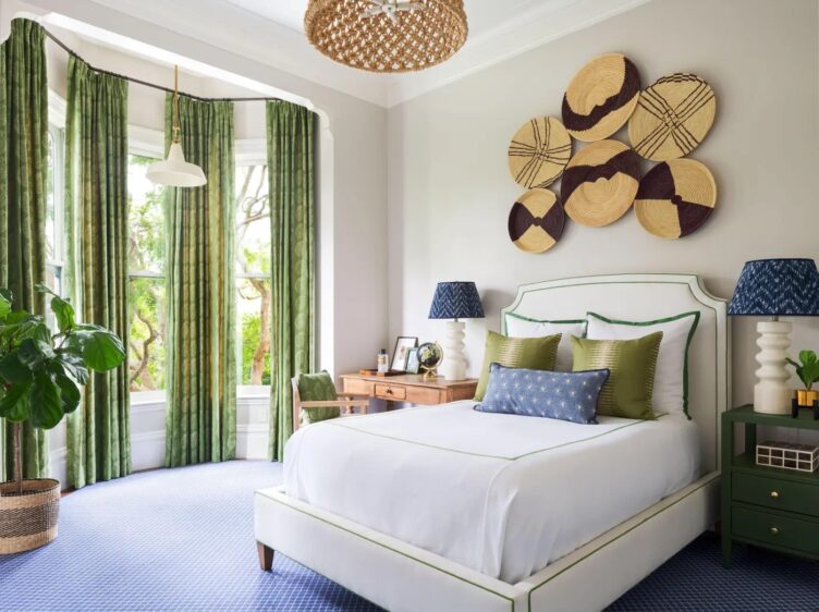 Wall baskets, a rattan chandelier, and a rattan planter fill this Presidio Heights guest room. Pops of green, a writing desk, and a set of bedside lamps finish the room. 