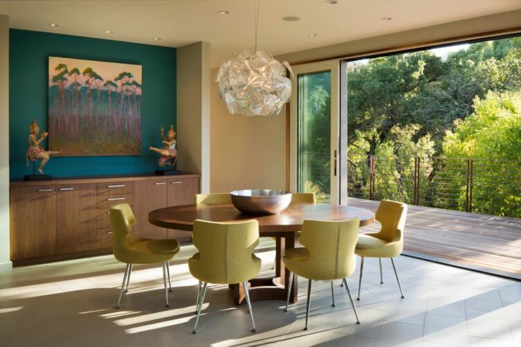 Mansfield + O'Neil used a round mid-century modern dining table and green mid-century dining chairs in this al fresco dining room. 