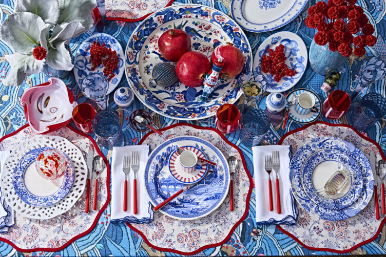 Red and blue holiday tabletop with simple centerpiece composed of plates and pomegranates  