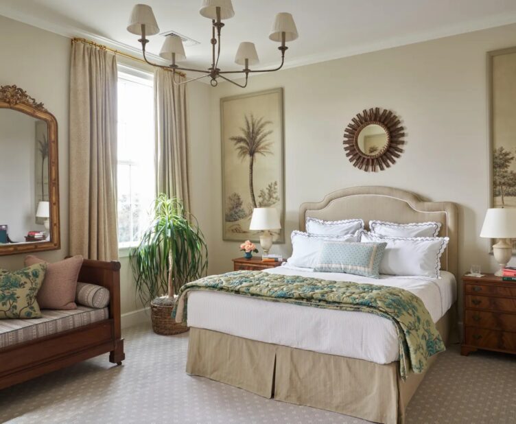 neutral bedroom with beige upholstered bed, sunburst mirror, wood bench, and potted ponytail palm