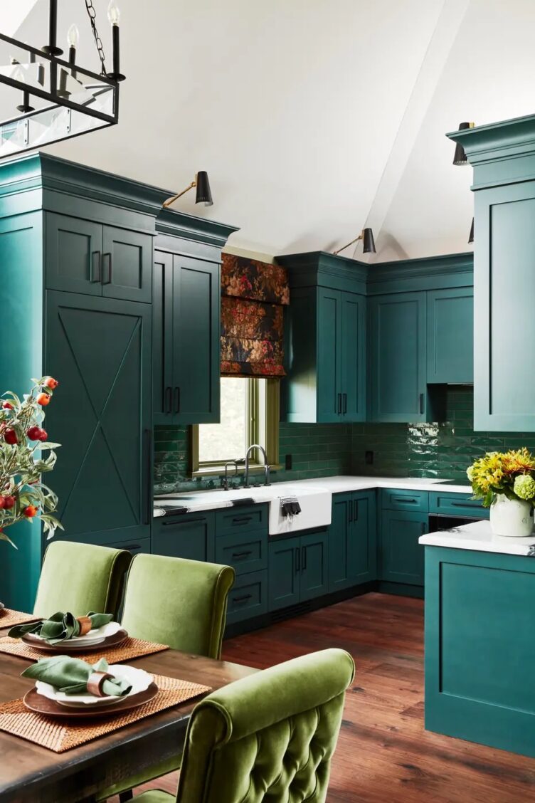  kitchen with Forest Green cabinets, green backsplash tile, green velvet chairs and black and brass sconces